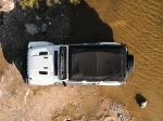 Namiot dachowy Wild Land Normandy Auto PRO 140 złożony na dachu białego Jeepa nad brzegiem rzeki, widok z góry.